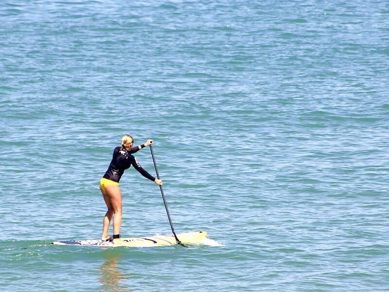 Une femme pagaie à la main pratique le paddle sur une mer d'huile