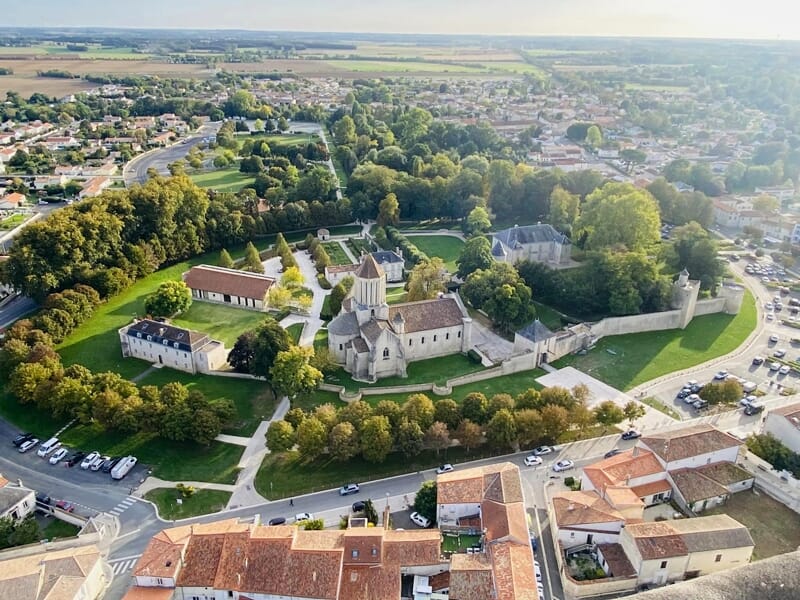 Vue aérienne d'un château fortifié entouré de murs, arbres verts et bâtiments anciens dans une ville.