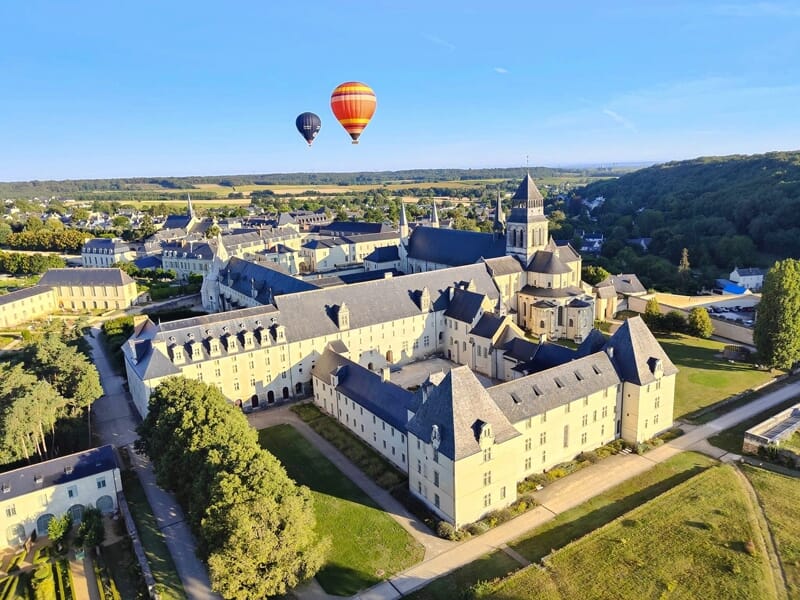 Vue aérienne d'un grand bâtiment historique avec deux montgolfières colorées dans un ciel clair au-dessus.