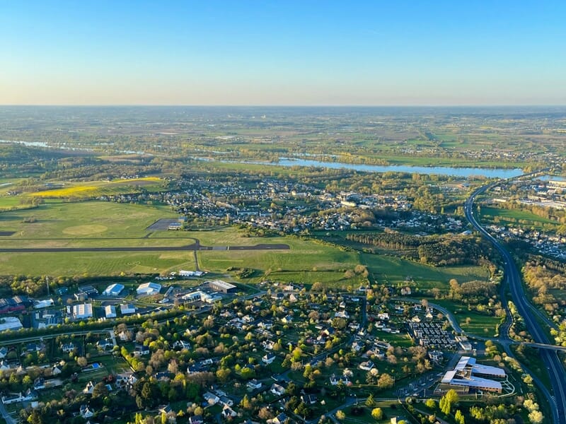 Vue aérienne d'une ville avec des routes, des maisons et des espaces verts sous un ciel dégagé.