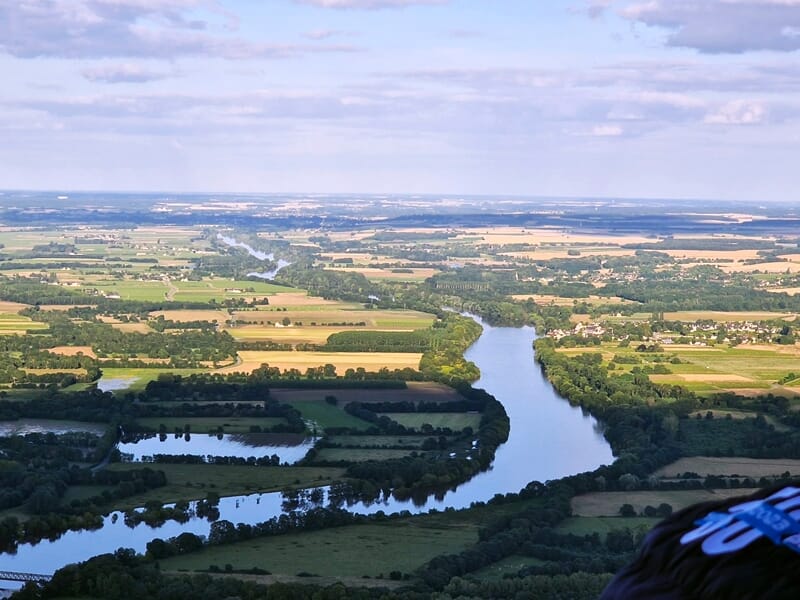 Paysage vu du ciel avec une rivière sinueuse traversant des champs verts et jaunes sous un ciel nuageux.