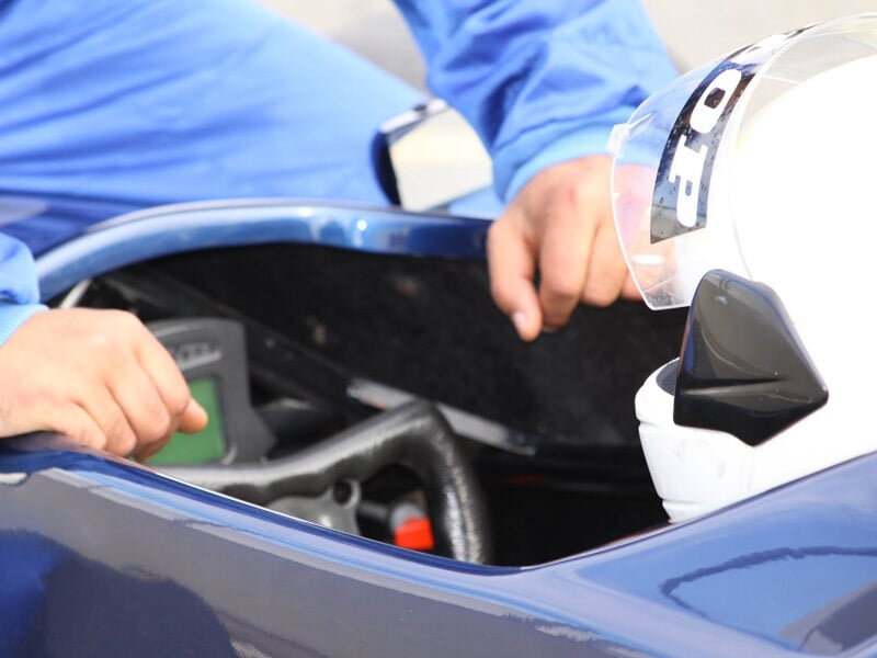 Vue rapprochée du tableau de bord et du casque blanc d'un pilote dans une monoplace bleue.
