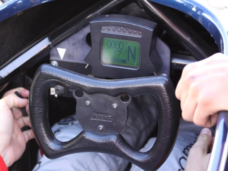 Volant de monoplace tenu par un pilote en combinaison blanche, prêt à piloter sur circuit.