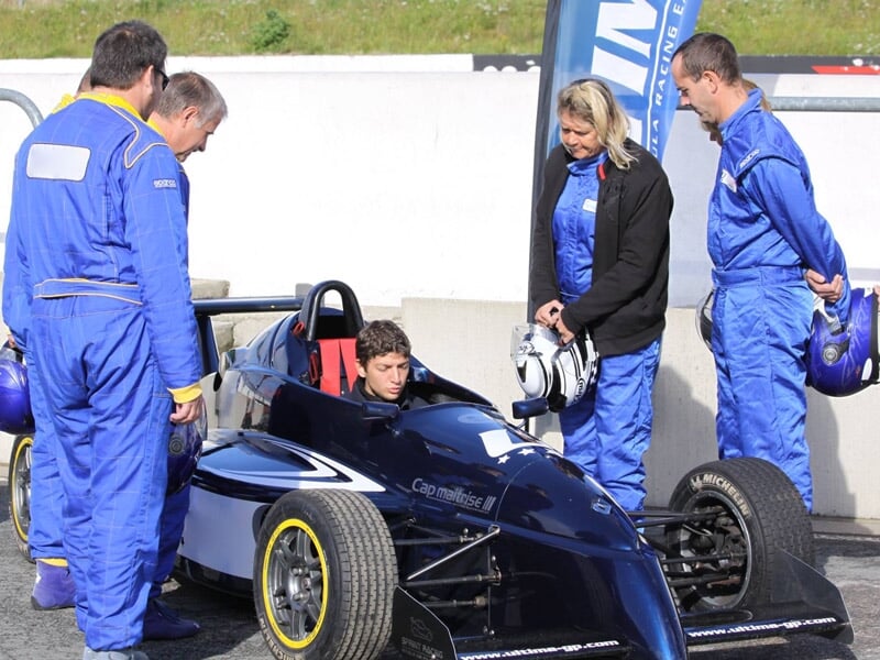 Groupe de personnes en combinaison bleue autour d'une monoplace noire sur le paddock avant la course.