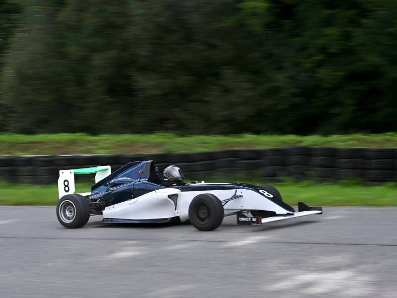 Monoplace blanche et bleue sur circuit de Haute Saintonge, pilotée par un conducteur casqué.