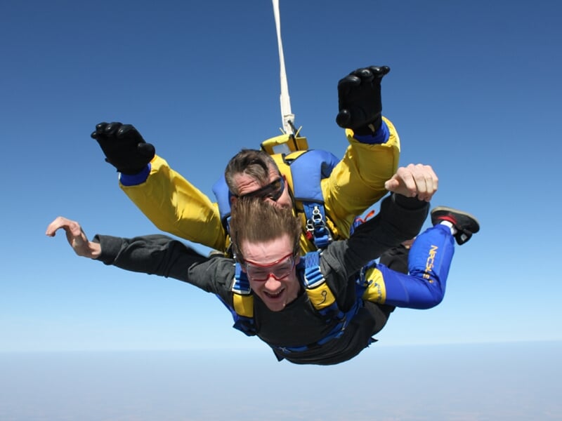 Saut en parachute en tandem avec un instructeur, les deux en chute libre dans un ciel bleu sans nuages.