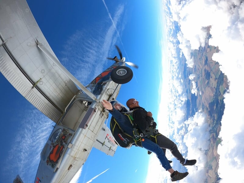 Saut en parachute en tandem avec parachute ouvert, deux personnes en chute libre au-dessus des champs.