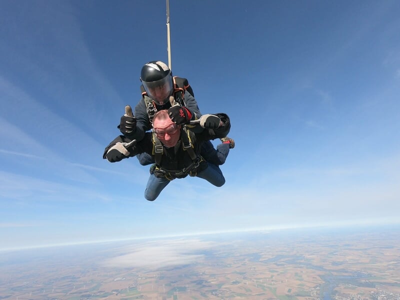 Saut en parachute en tandem, deux personnes en chute libre, ciel bleu clair et nuages blancs en arrière-plan.