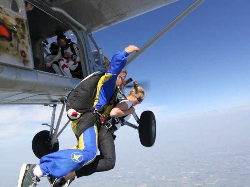 Deux personnes en combinaison de saut en parachute sautant ensemble hors d'un avion en plein ciel bleu.