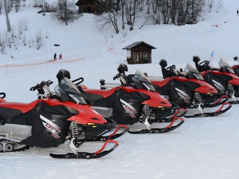Rangée de motoneiges rouges et noires alignées sur la neige avec une petite cabane en arrière-plan.