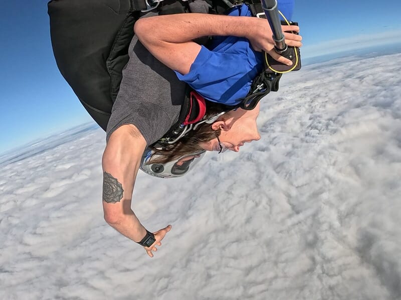 Personne en chute libre lors d'un saut en parachute au-dessus des nuages, vue plongeante sur un ciel bleu clair.