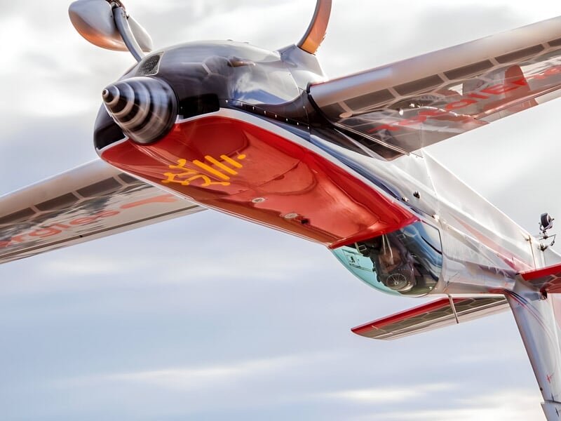 Vue dynamique d'un avion acrobatique en vol, avec une hélice en mouvement et un ciel légèrement nuageux en arrière-plan