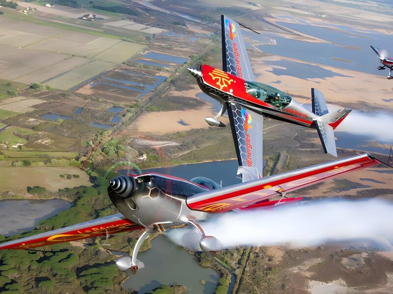 Vue sur trois avions de voltige en pleine acrobatie au-dessus d'un paysage agricole