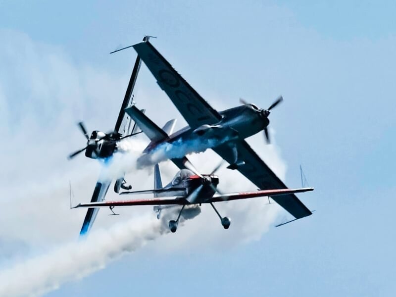 Trois avions acrobatiques équipés de fumigènes exécutant une manœuvre rapprochée en vol, avec un ciel nuageux en arrière-plan