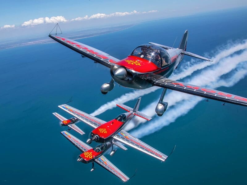 Quatre avions de voltige rouges et gris volent en patrouille au-dessus de l'océan