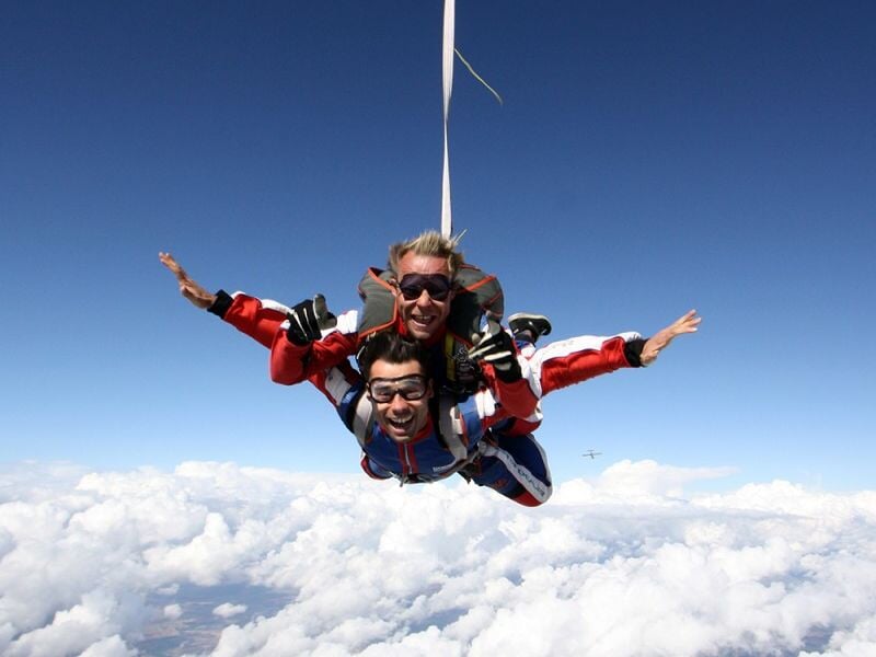 Saut en parachute en tandem au-dessus des nuages, les deux personnes ont les bras écartés.