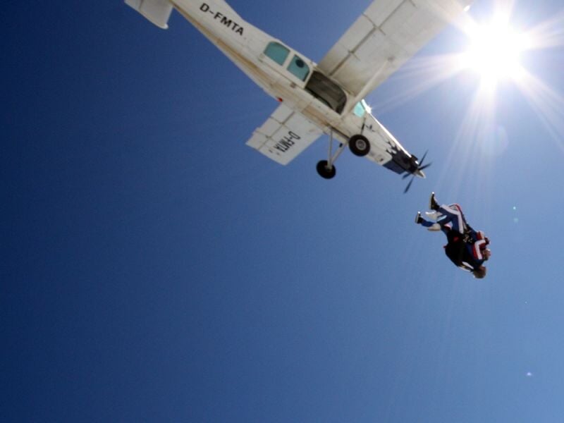 Parachutiste en chute libre s'éloignant d'un petit avion blanc sous un ciel bleu clair.