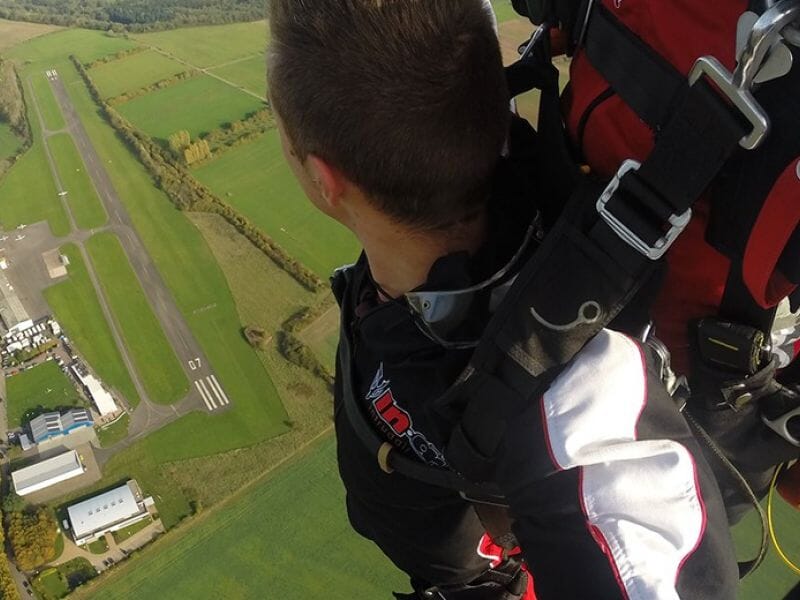 Vue aérienne d'une personne en parachute lors d'un saut au-dessus d'une piste d'atterrissage et de champs verts