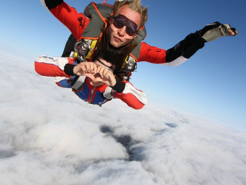Parachutiste en tandem en chute libre au-dessus des nuages, ciel bleu clair et nuages blancs.