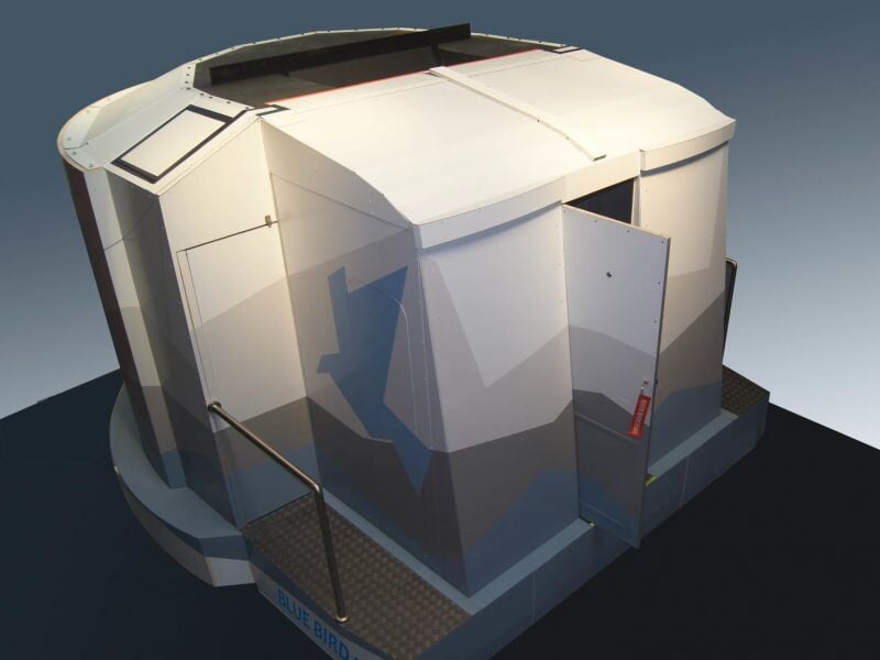 Simulateur de pilotage d'avion blanc avec structure fermée et porte ouverte sur un fond neutre.