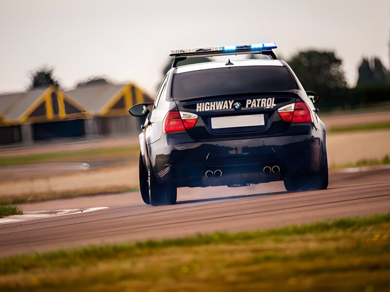 Voiture de patrouille autoroutière noire et blanche vue de l'arrière sur circuit avec fumée aux roues.