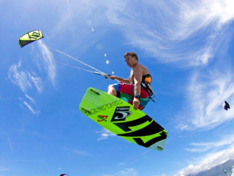 Kitesurfeur en plein saut avec une planche verte et une voile verte sur un ciel bleu clair avec quelques nuages.