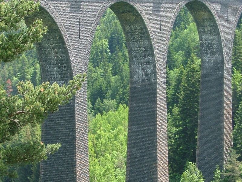 Gros plan sur les arches du viaduc en pierre, mettant en valeur les détails architecturaux et la forêt environnante