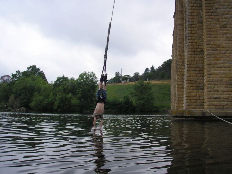 Saut à l'élastique avec une immersion dans l'eau, l'homme touchant la surface de la rivière en étant suspendu la tête en bas, sous un ciel nuageux