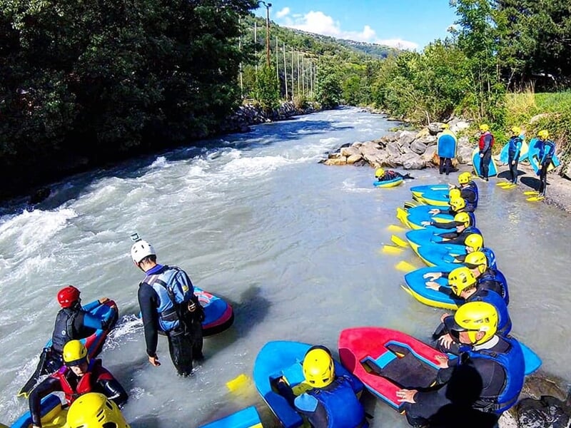 Groupe de personnes équipées de casques et combinaisons prêtes pour une activité d'hydrospeed en rivière.