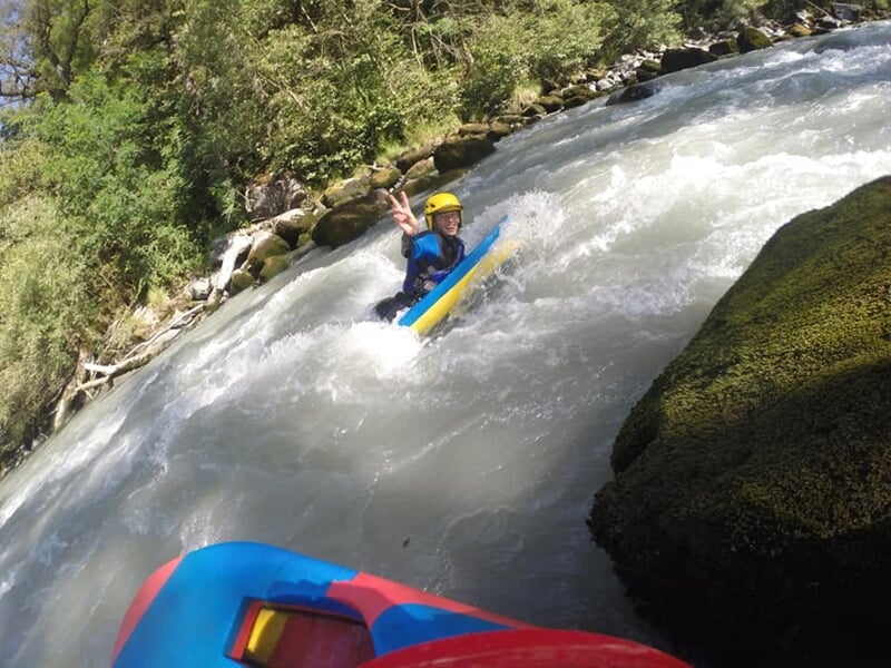 Pratiquant d'hydrospeed en rivière en eau vive, faisant un signe de paix avec la main en descendant les rapides.