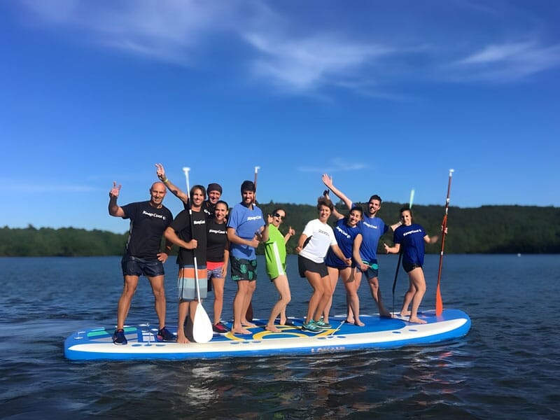 un groupe de 10 personnes se tiennent debout sur un paddle géant au milieu du lac