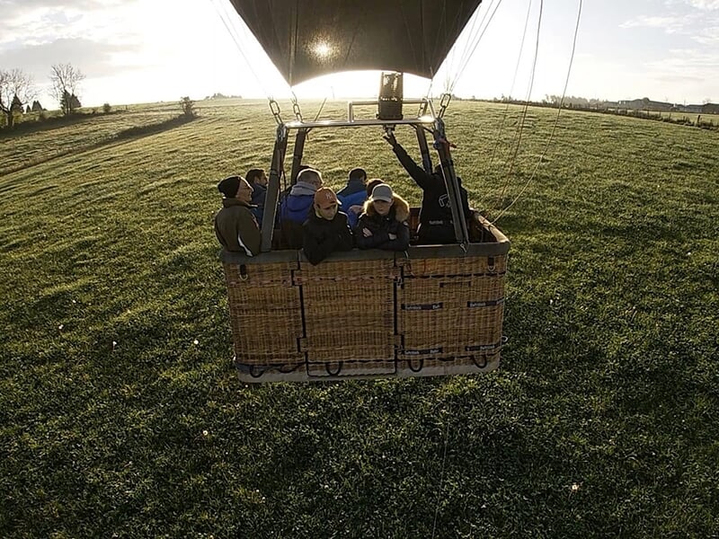 Un groupe de passagers dans une nacelle de montgolfière Montgolfière en vol avec plusieurs passagers au-dessus d’un champ verdoyant au lever du jour.un champ au lever du soleil.