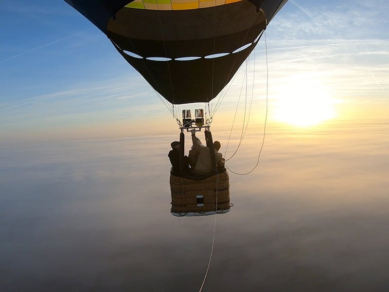 Montgolfière flottant au-dessus des nuages avec un ciel doré au lever du soleil.