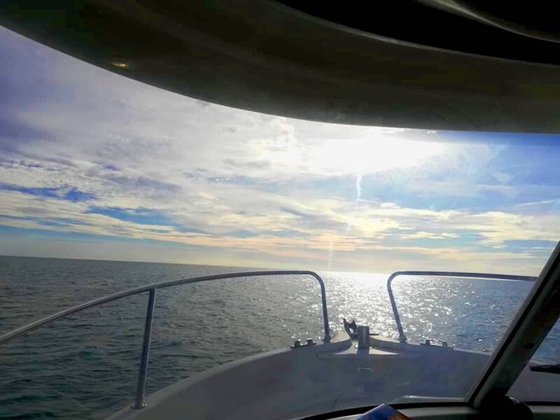 Vue depuis un bateau sur la mer avec un ciel partiellement nuageux et le soleil brillant à l'horizon.