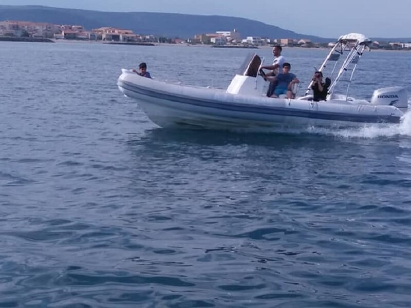 Un bateau pneumatique gris avec plusieurs passagers naviguant sur une mer calme avec des collines en arrière-plan.