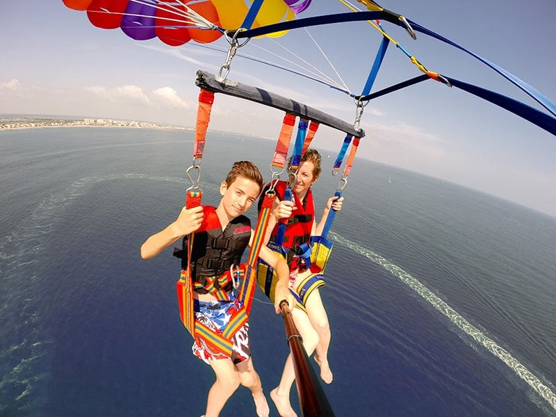 Deux personnes en parachute ascensionnel suspendues à un parachute coloré au-dessus de la mer sous un ciel clair.