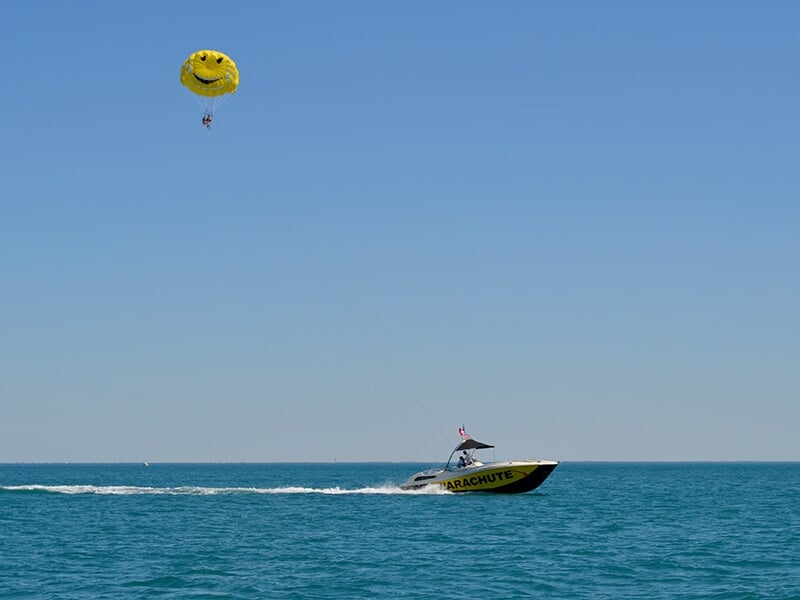 Un bateau rapide tractant un parachute jaune souriant avec une personne en parachute au-dessus de la mer bleue.