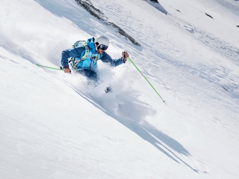 Skieur en tenue bleue dévalant une pente enneigée avec des bâtons de ski verts dans la poudreuse fraîche.