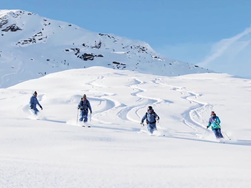 Quatre skieurs en randonnée hors-piste progressant côte à côte sur une large étendue de neige vierge.