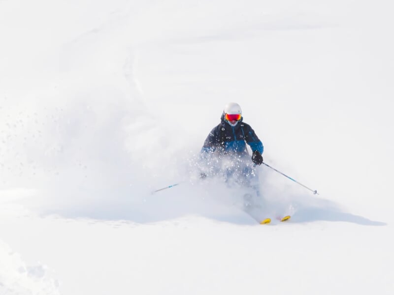 Skieur solitaire en combinaison sombre traversant une profonde neige poudreuse sous un ciel clair.