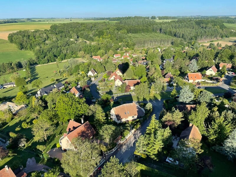Vue aérienne d'un village avec des maisons et des arbres sous un ciel bleu clair et lumineux.