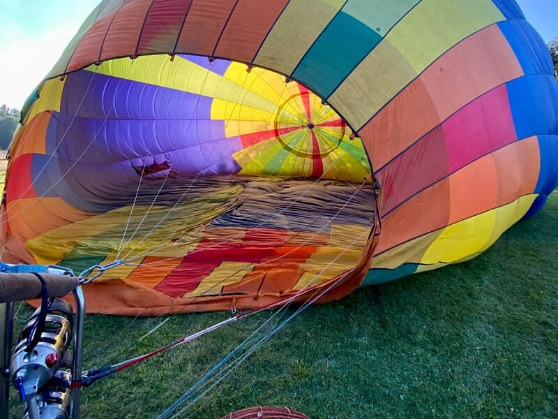 Montgolfière multicolore en cours de gonflage sur une pelouse verte avec un ciel clair en arrière-plan.