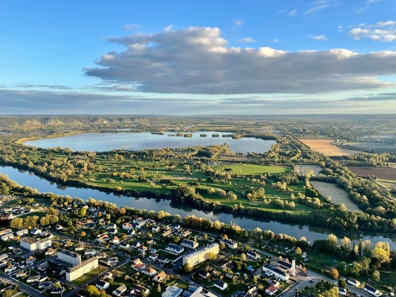 Vue panoramique d'une ville au bord d'un lac avec des îles et des espaces verts sous un ciel partiellement nuageux.