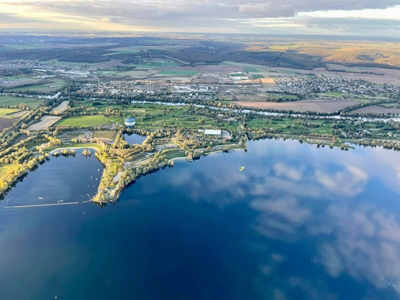 Lac vaste reflétant le ciel bleu avec des collines et des zones urbaines autour au coucher du soleil.