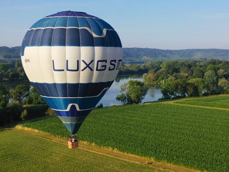 Groupe de personnes souriantes dans la nacelle d'une montgolfière au-dessus d'un paysage fluvial.