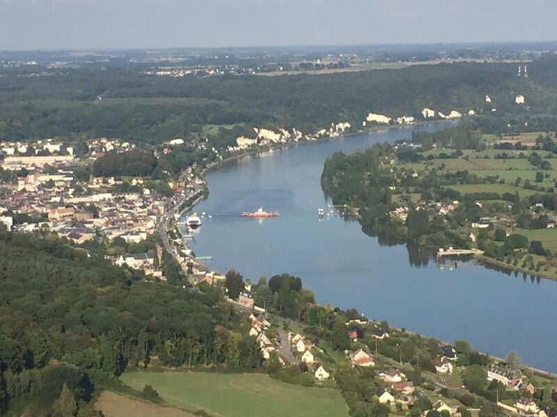 Vue aérienne d'une rivière sinueuse bordée de maisons et de forêts sous un ciel clair et lumineux.