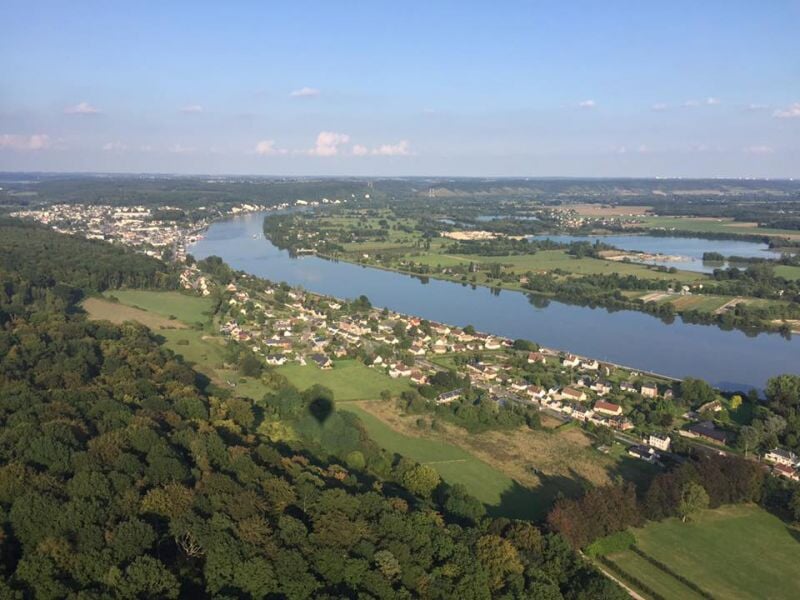 Panorama aérien d'une rivière entourée de forêts et de maisons dispersées dans un paysage verdoyant.