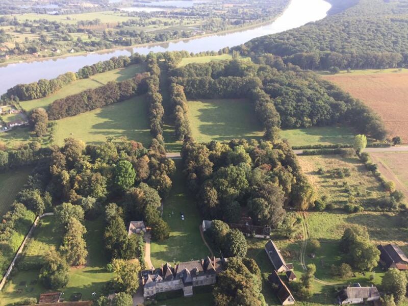 Vue aérienne d'un domaine avec un grand bâtiment ancien entouré d'arbres et de champs verts.