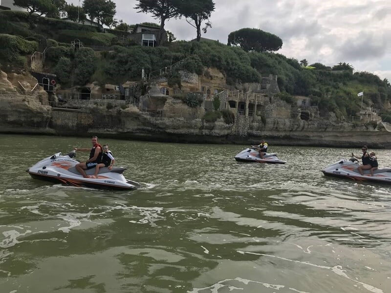 Trois personnes conduisent des jets skis sur une rivière entourée de falaises et de végétation verte.