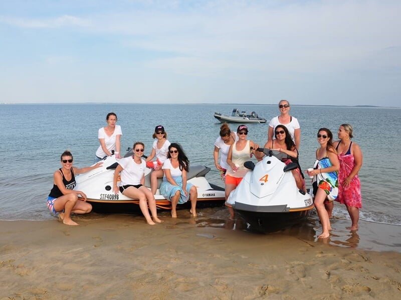 Groupe de neuf personnes posent sur deux jets skis sur une plage, souriants et prêts pour une sortie.